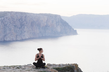 Woman practicing pose from yoga on the edge of the cliff meeting