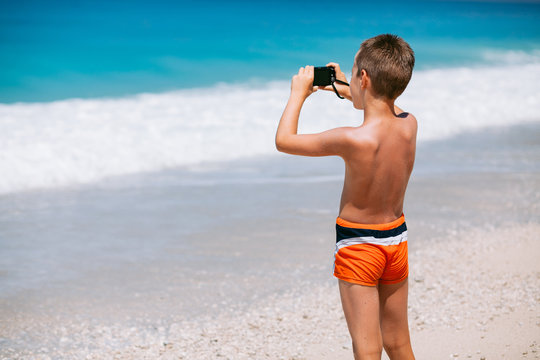 Beach vacation dream. Handsome young boy enjoying in beautiful tropical beach and taking some photos with his camera.