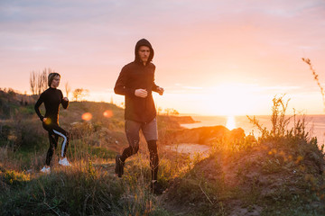 Fototapeta na wymiar woman and man running on beach. Fit young fitness couple exercising during sunrise or sunset 