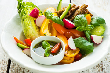 Delicious fresh sliced organic vegetables with homemade pesto on the plate and on the wooden background