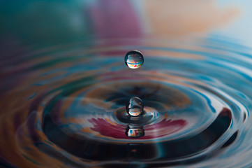 Macro photo of water drops falling into a pool of water, causing a splash and ripples.