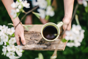 Green coffee cup on a wooden stand in the blossoming garden