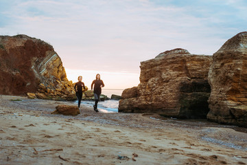 woman and man running on beach. Fit young fitness couple exercising during sunrise or sunset 