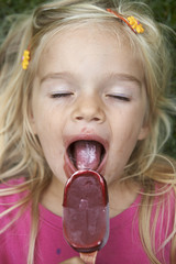 Beautiful little child blond girl eats - licking icecream in the summer