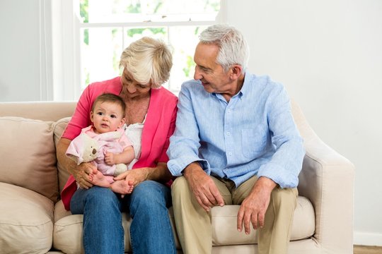 Happy grandparents looking at baby while siting on sofa