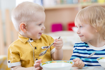 Two funny smiling very positive kids eating in kindergarten