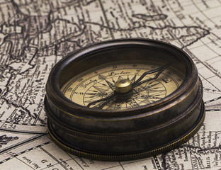 The old brown metal compass on a world map background.