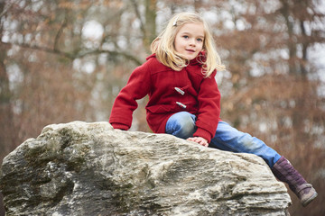 A cute five year old blond girl posing on a rock outside 