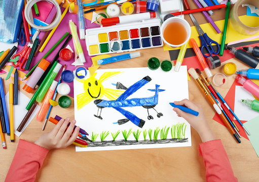 passenger airplane fly under sun child drawing, top view hands with pencil painting picture on paper, artwork workplace