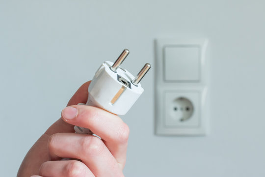Hand mit Stecker, Steckdose im Hintergrund