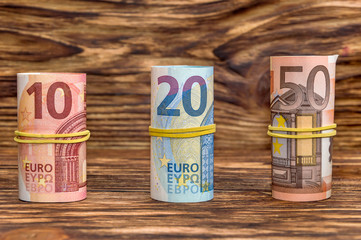 Ten, twenty and fifty euro rolled up on wooden background