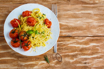 Pasta with small cherry tomatoes baked with garlic, salt and olive oil. White plate on wooden background. Top view.