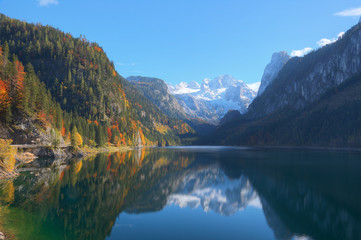 Fototapeta na wymiar Autumn scenery of Lake Gosausee with snow-capped Dachstein Mountain in the background and beautiful reflections on the smooth water, in Gosau, Austria ~ A brisk fall scenery of Alps, Europe.