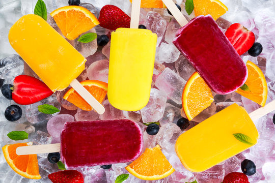 refreshing fruit popsicle lollies on ice background with berries, peppermint.