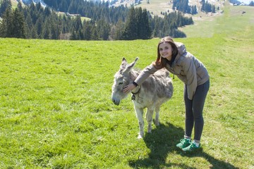 Fototapeta premium Beautiful girl stroking a donkey. Holidays in the mountains. Girl on the mountain meadows. 