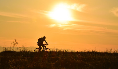 Cyclist on sunset sky with clouds