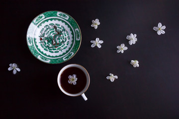 cup of black tea, a saucer with an image of a dragon, white flowers on a dark background