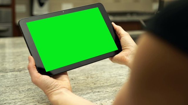 A female holding a tablet with green screen in modern kitchen.  