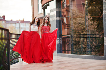 Portrait of two fashionable girls at red evening dress posed bac