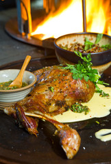Delicious free range roasted goat shoulder served on a rustic metal plate by a hot open coal fire....