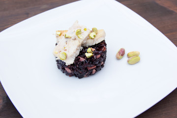 Black rice with fish and pistachios on a wooden table seen up close