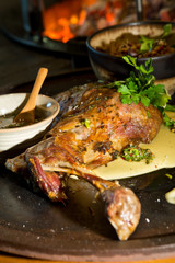 Delicious free range roasted goat shoulder served on a rustic metal plate by a hot open coal fire. Served with fresh parsley.