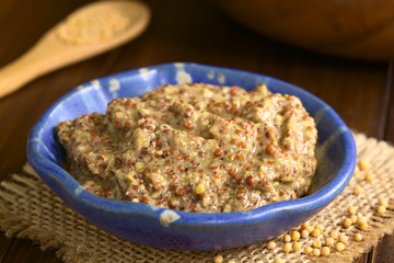 Rotisseur oder Körniger Senf in kleiner Schüssel, gelbe Senfkörner an der Seite, fotografiert mit natürlichem Licht (Selektiver Fokus, Fokus ein Drittel in den Tafelsenf)
