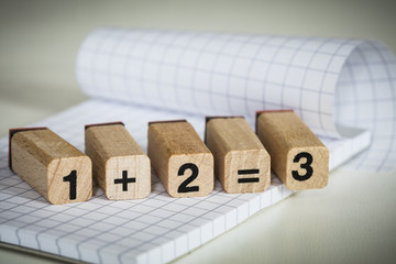 wooden stamps showing the mathematical function of 1 + 2 = 3 on paper block
