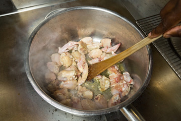Organic chicken wings being cooked in a pan of hot frying oil, stirred with a wooden spoon.