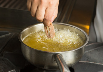 Calamari ring being placed into a pan of hot bubbling oil.