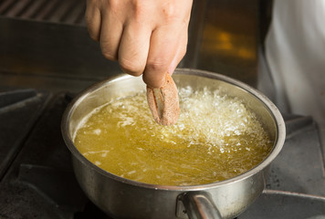 Calamari ring being placed into a pan of hot bubbling oil.