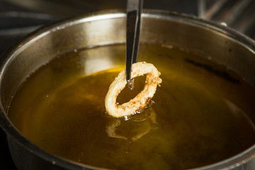 Lightly fried Calamari ring being taken out of a pan of hot oil.