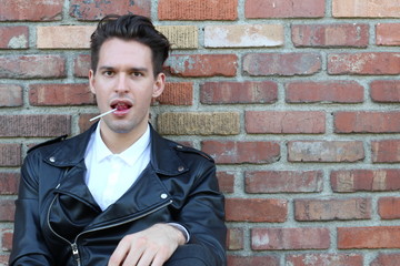 Man licking a pink shiny lollipop. Close up against red brick wall background.