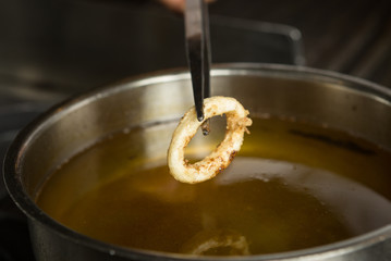 Lightly fried Calamari ring being taken out of a pan of hot oil.