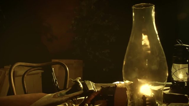 Scene tracks down to guns and bullets from the old American wild west era lying on a table lit by an oil lamp.