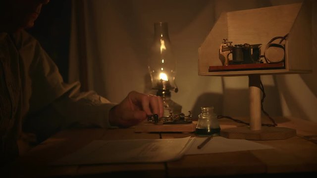 A telegrapher from the old American west era in a in a dimly lit tent sends a telegraph message.