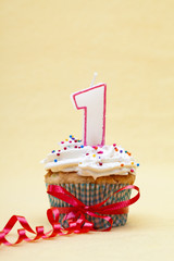 close-up image of a cupcake with number 1 candle and streamer.