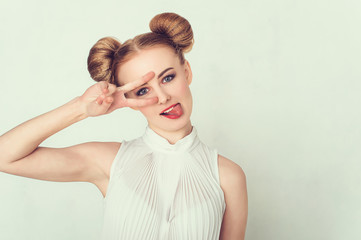 Beautiful girl with funny hairstyle makes peace sign hands, smiling and showing tongue.