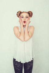 Portrait of surprised beautiful girl with funny hairstyle holding her head in amazement and open-mouthed. 