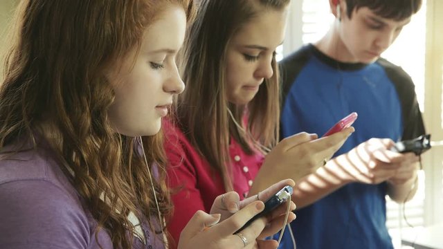 Three teens using smart phones to find music and communicate with friends.