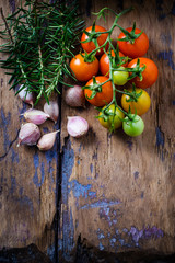 Cherry tomatoes, garlic and rosemary on wooden background