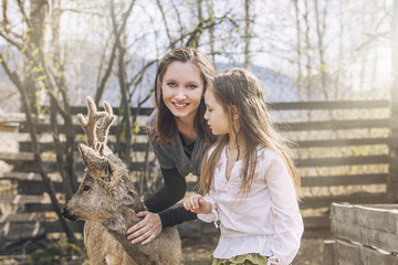 Fototapeta premium Beautiful little girl and her mom hugging animal ROE deer in the
