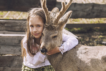 Obraz premium Beautiful little girl hugging animal ROE deer in the sunshine