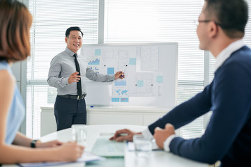 Smiling Asian businessman conducting presentation in front of colleagues