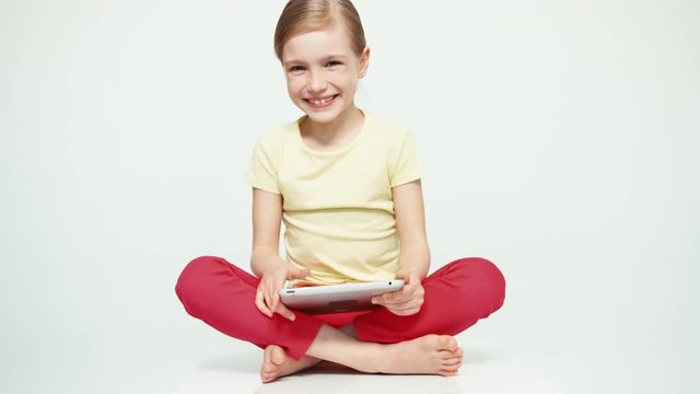 Cute girl 7-8 years old using tablet pc on white background and smiling at camera