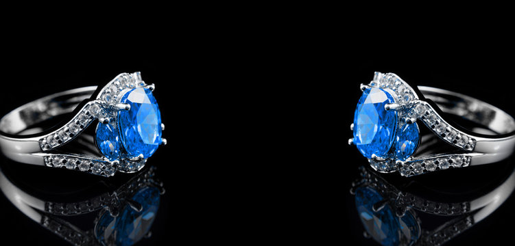 Luxury jewelry. White gold or silver engagement rings with colored gemstone closeup on black background with space for your text. Selective focus.