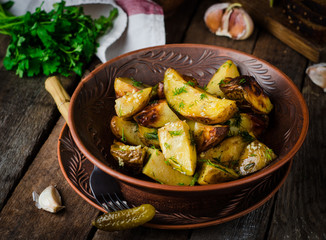 Roasted potatoes with garlic and fennel in clay bowl on wooden background. Selective focus