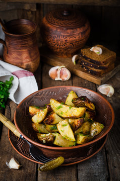 Roasted potatoes with garlic and fennel in clay bowl on wooden background. Selective focus