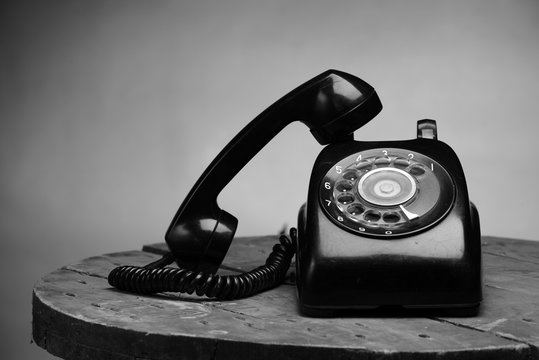 Old black phone with dust and scratches, isolated on wooden retro floor