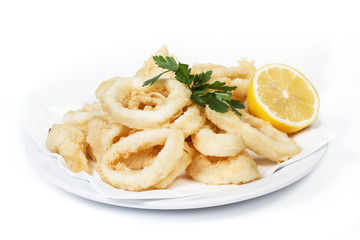 Calamares a la romana con unas hojas de perejil y medio limón en un plato redondo blanco sobre un...